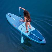 Femme debout sur SUP gonflable Selka 10' bleu pétrole Aquadesign, vue du dessus, lac calme